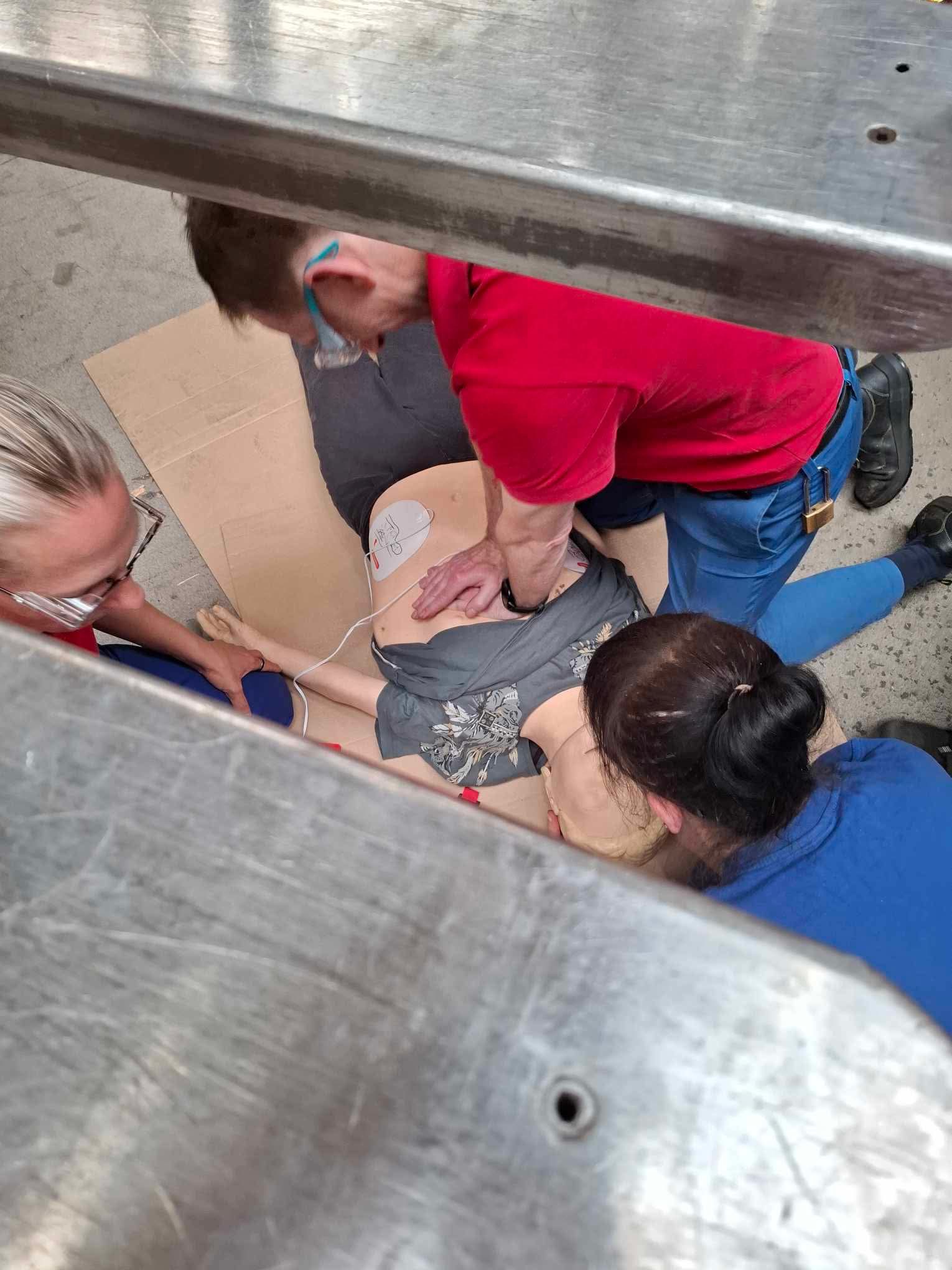Instruktorzy podczas praktycznego kursu pierwszej pomocy, wykonują resuscytację krążeniowo-oddechową na manekinie, widok z góry z perspektywy drabiny.