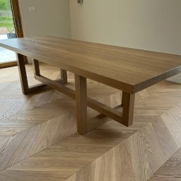 Mazurska Pracownia Drewna - Stół z jasnego drewna o prostokątnym blacie i geometrycznych nogach, ustawiony na parkiecie w jodełkę, widok z perspektywy podłogi.