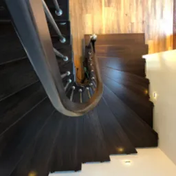 Spiralne schody z ciemnego drewna z metalową poręczą, oświetlone punktowymi lampami podłogowymi i ściennymi. Widok z góry podkreśla kręty kształt i nowoczesny design.