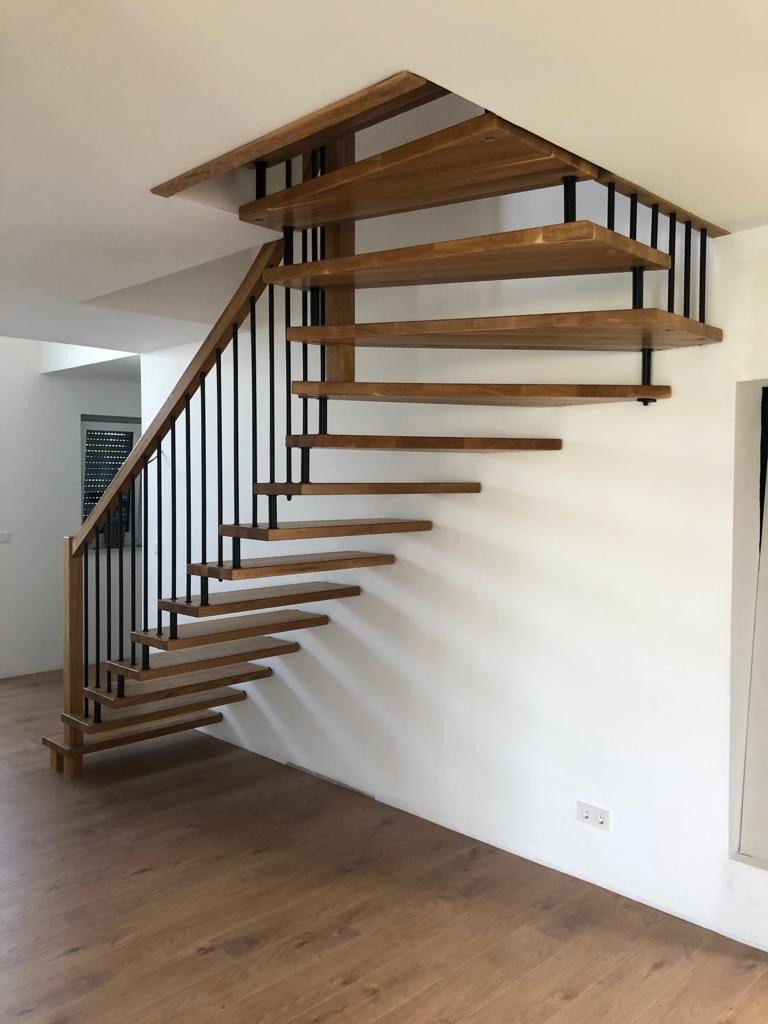 Nowoczesne schody drewniane z czarnymi, metalowymi wspornikami, stopnie bez podstopnic, drewniana poręcz, jasne wnętrze.
