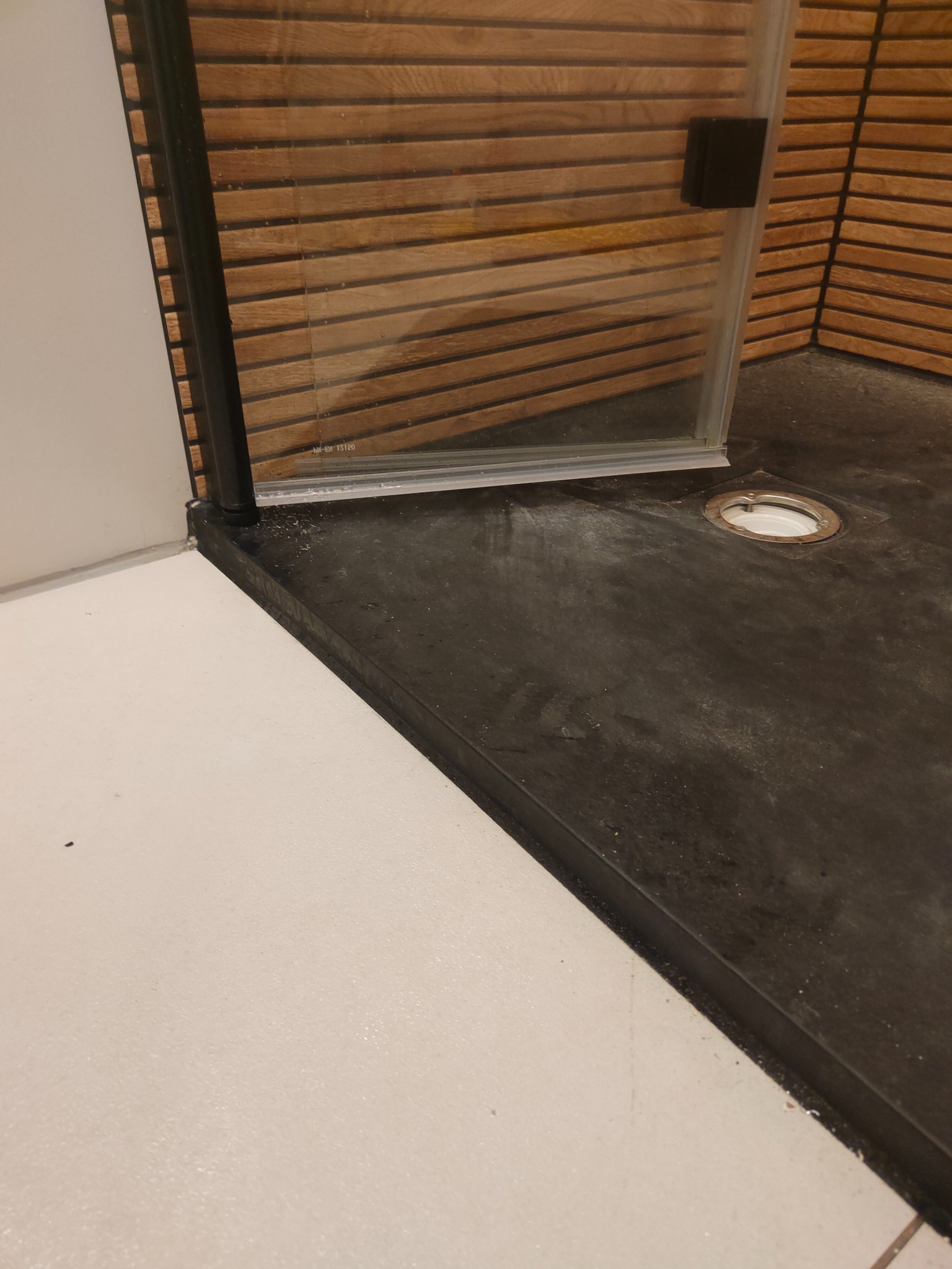 Nowoczesny brodzik z odpływem liniowym i kabiną prysznicową z drewnianymi panelami. Minimalistyczny design, czarno-biała kolorystyka, ukończony etap prac.