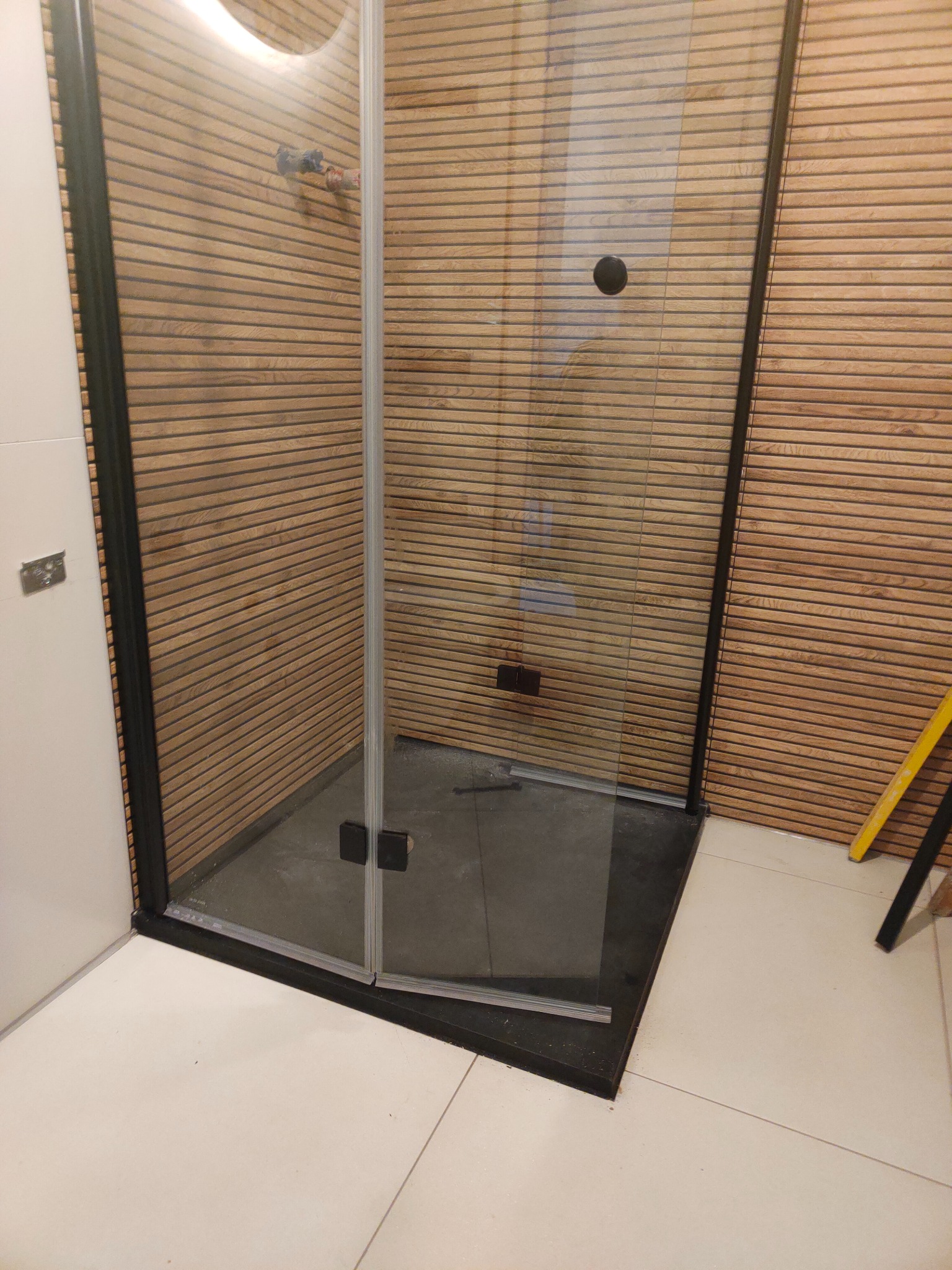 Kabina prysznicowa z czarnymi profilami i drewnopodobnymi panelami ściennymi. Widoczny fragment poziomicy. Nowoczesny design.