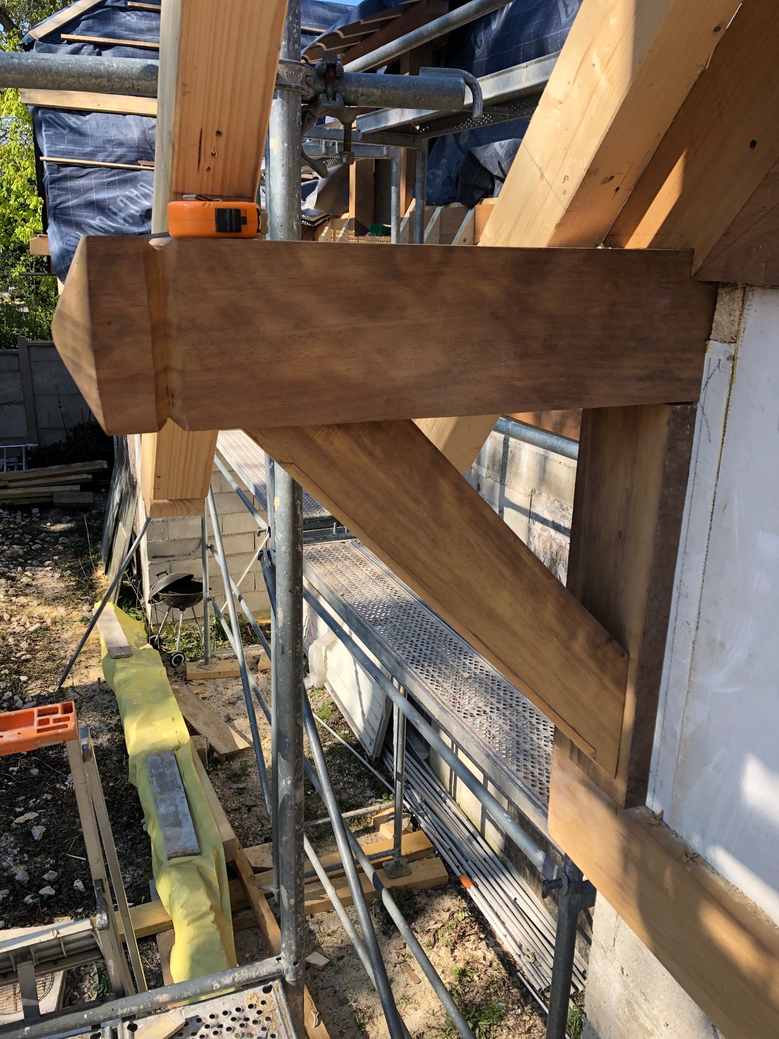 Fragment konstrukcji domu szkieletowego w trakcie montażu, widoczne drewniane belki, rusztowanie i częściowo ocieplona ściana zewnętrzna.