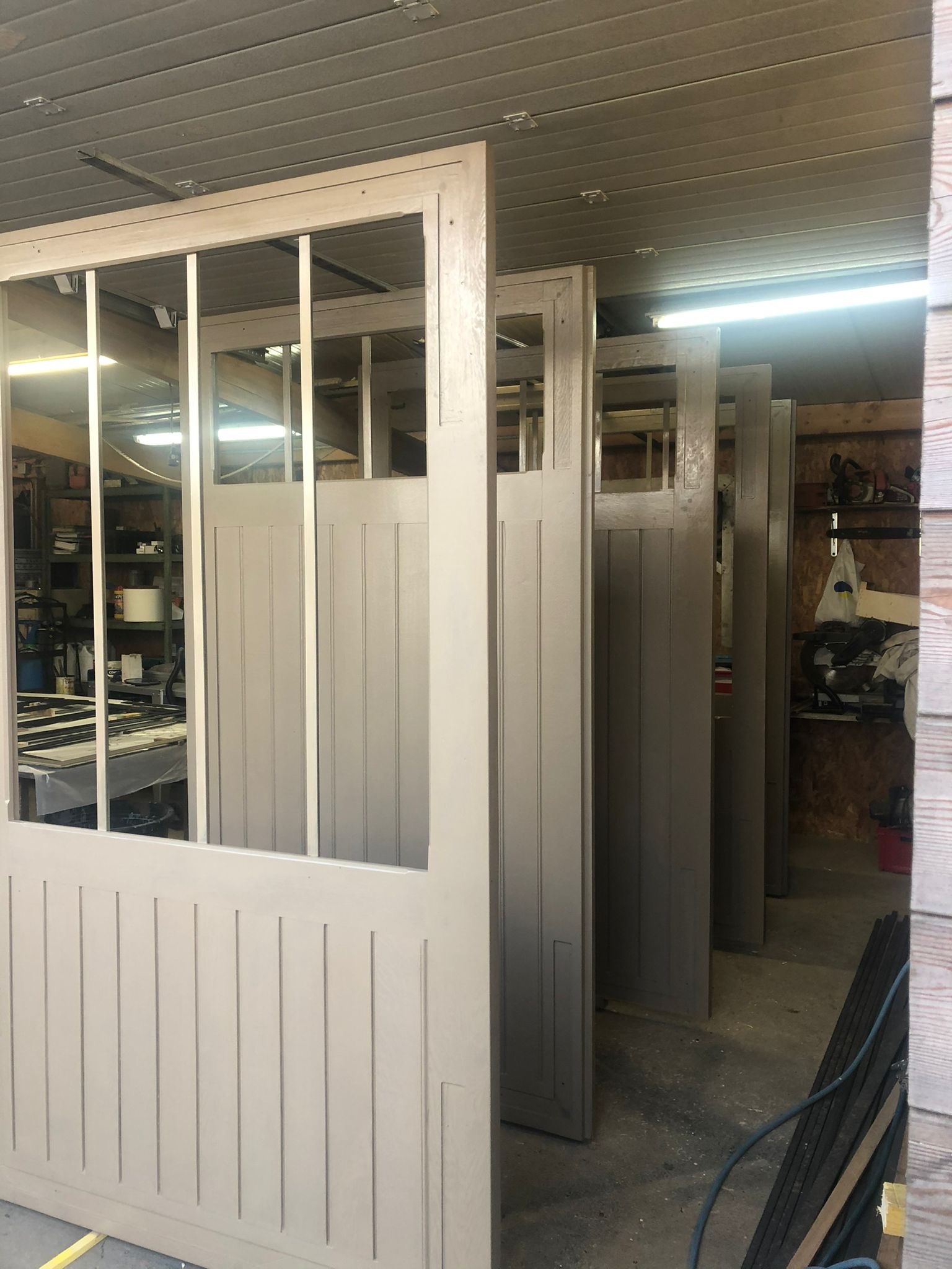 Szereg beżowych, niedokończonych elementów konstrukcyjnych z drewnianą ramą i panelami w warsztacie, prawdopodobnie do budowy ścian lub elewacji.