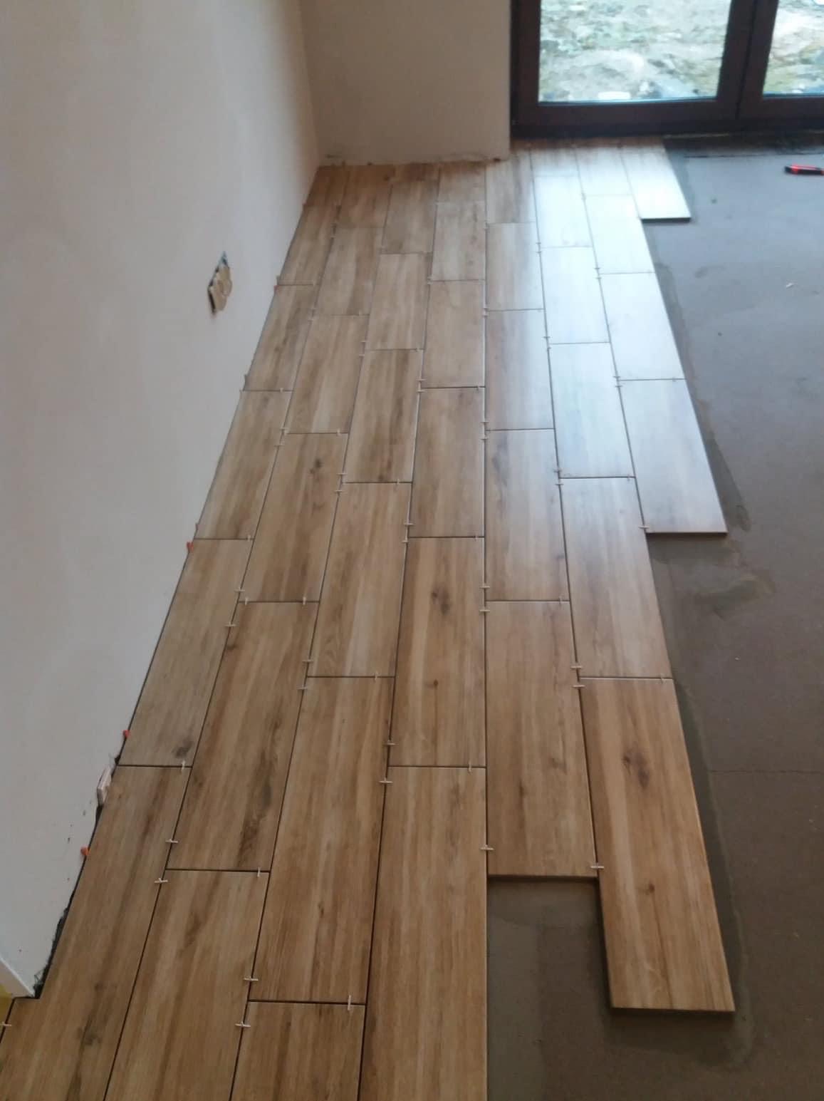 Układanie podłogi z płytek imitujących drewno w trakcie remontu, widoczne plastikowe krzyżyki dystansowe i niedokończona powierzchnia.