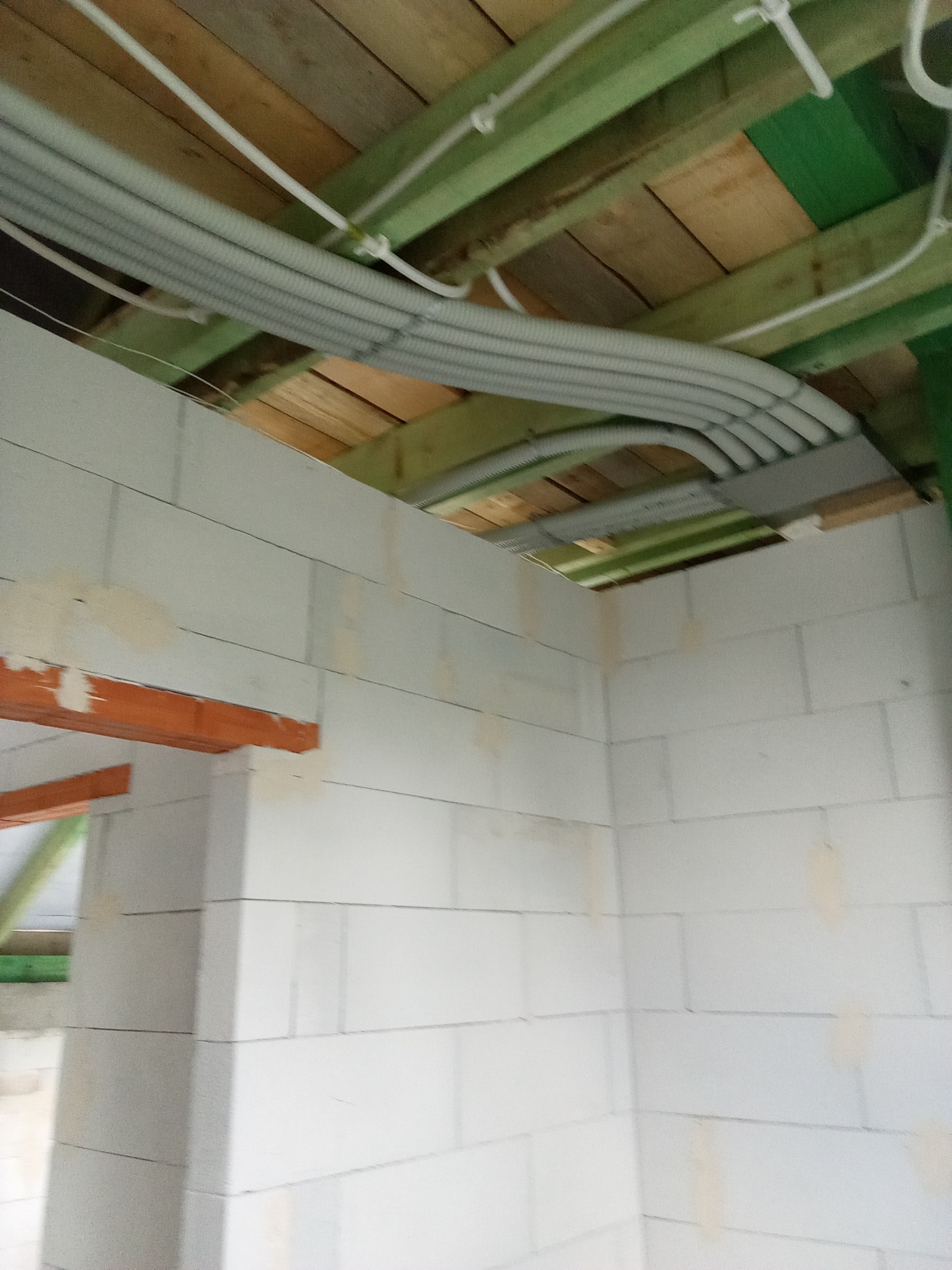 Szereg szarych, elastycznych rur wentylacyjnych przymocowanych do drewnianego stropu w surowym wnętrzu z białych bloczków.