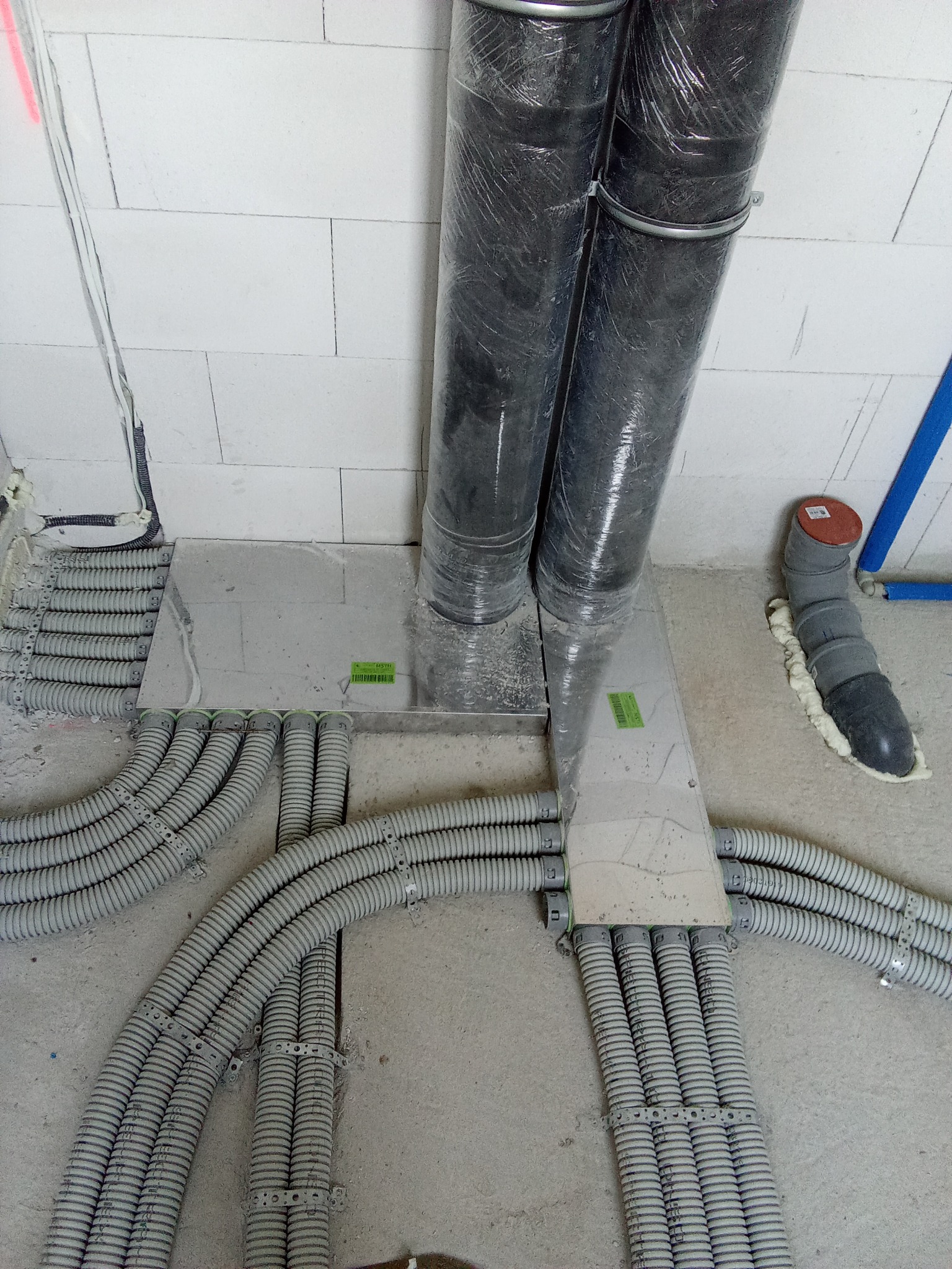 Rozprowadzenie rur wentylacyjnych w folii ochronnej oraz peszli instalacyjnych na surowym podłożu, widoczne mocowania i elementy uszczelniające.