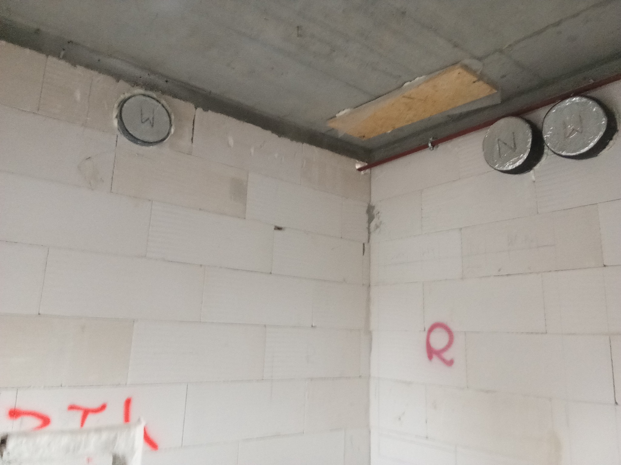 Surowy stan wnętrza z widocznymi otworami w ścianach z betonu komórkowego, zabezpieczonymi folią i oznaczone literami W i N, oraz czerwonymi oznaczeniami na ścianach.