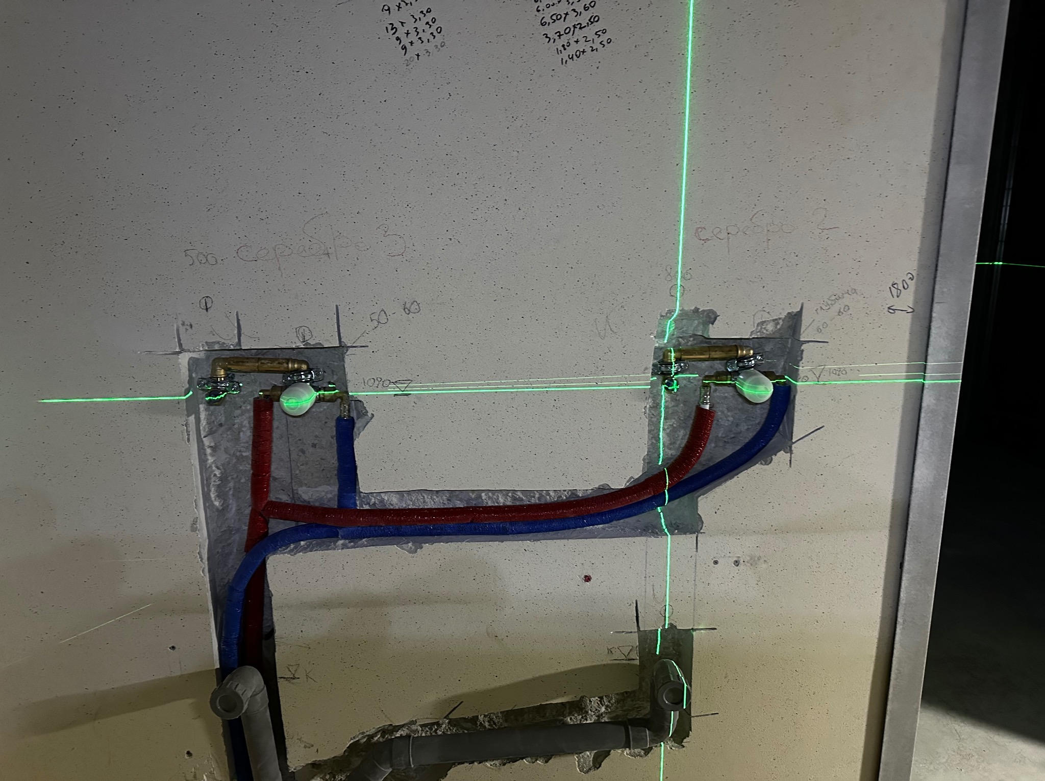 Świeżo zamontowane zawory z rurami doprowadzającymi ciepłą i zimną wodę w bruzdach ściany, wyznaczane laserowym poziomem.