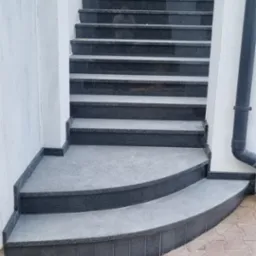 Granitowe schody zewnętrzne z zaokrąglonymi stopniami prowadzące do drzwi wejściowych w Łękach, wykończone ciemnoszarym kamieniem.