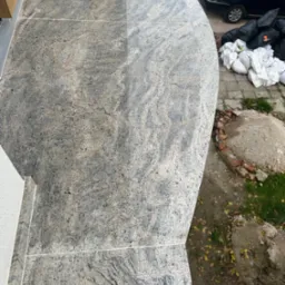 Wykończony taras z szarej, wzorzystej płyty kamiennej, widok z góry, z elementami otoczenia: samochód, worki, ziemia.