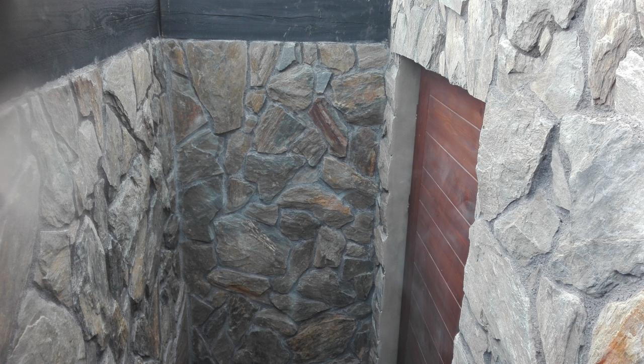 Kamienna okładzina ściany z nieregularnych szarych kamieni, widoczna drewniana belka stropowa i fragment drewnianych drzwi.