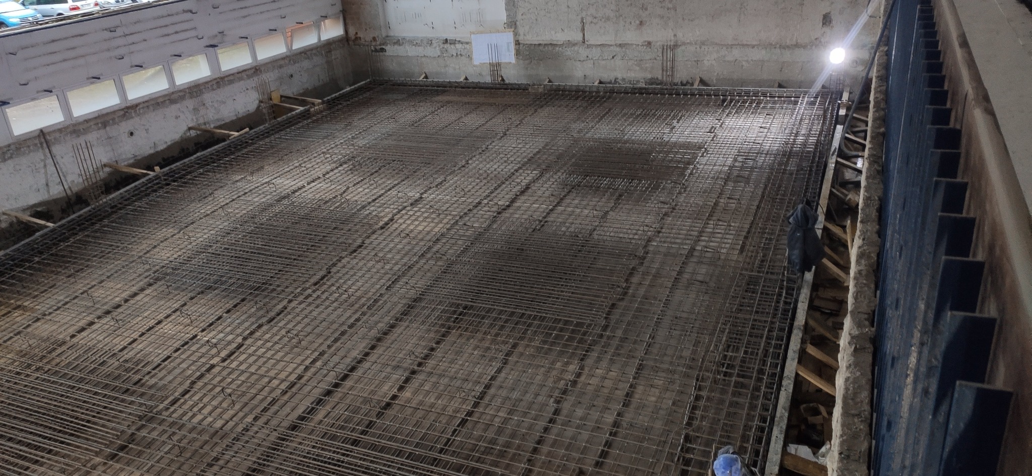 Zbrojenie fundamentu z siatki stalowej, przygotowane do zalania betonem, widok z góry w surowym wnętrzu budynku.