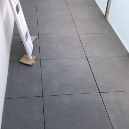 Black Gloves - Szare płytki na balkonie po remoncie, zabezpieczone kartonem pod drabiną, z widocznym kartonem po urządzeniu AGD.