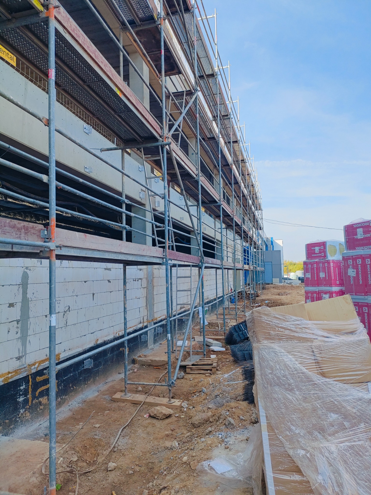 Budynek w trakcie budowy z rusztowaniem, widoczne materiały izolacyjne ROCKWOOL w oryginalnych opakowaniach