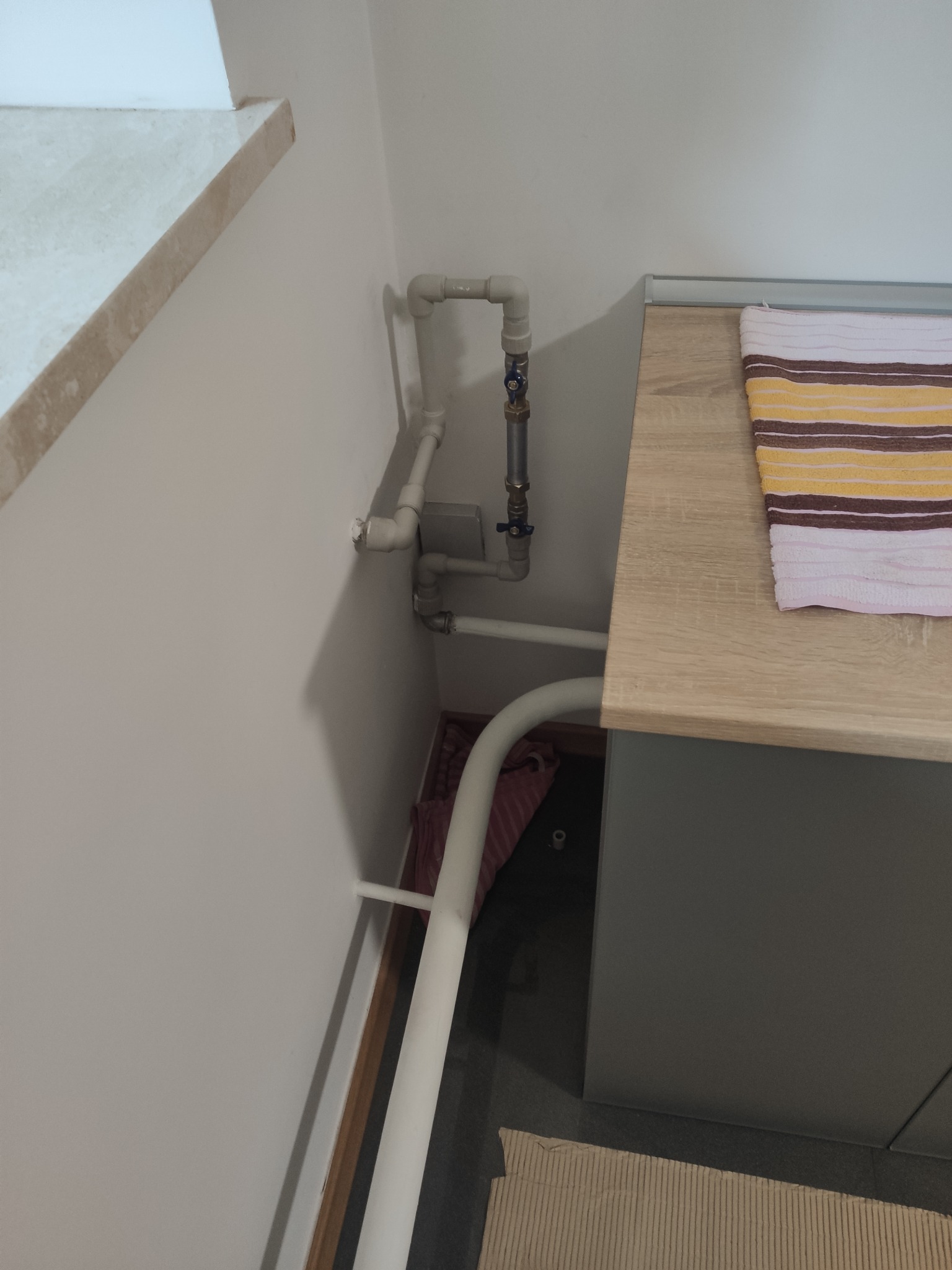 Szare rury instalacji gazowej z zaworami przy ścianie obok szafki z blatem i ręcznikiem w paski. Widoczne łączenia i elementy mocujące.