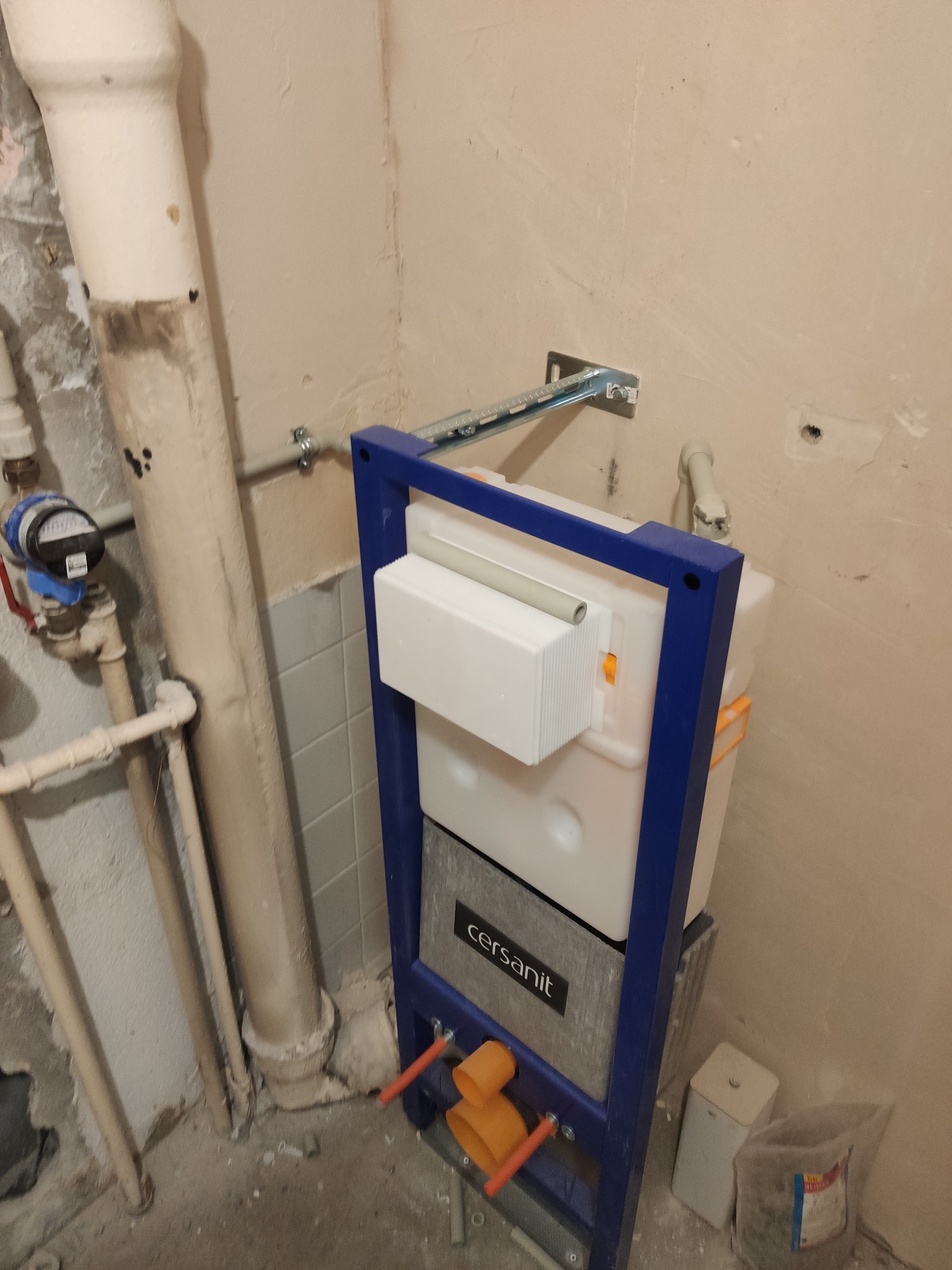 Stelaż podtynkowy Cersanit zamontowany przy ścianie z widocznymi rurami i licznikiem wody. Element instalacji hydraulicznej w trakcie montażu.