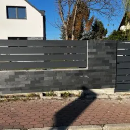 Nowoczesna brama wjazdowa z furtką, wykonana z szarego metalu i kamienia łupanego, z widocznym adresem budynku i tablicą uliczną 'Krawiecka'.