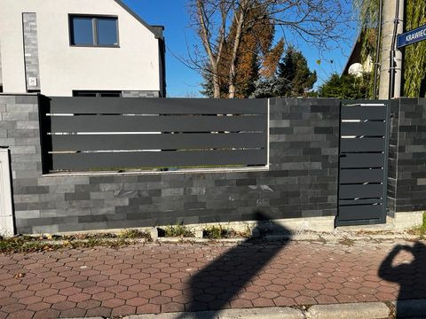Nowoczesna brama wjazdowa z furtką, wykonana z szarego metalu i kamienia łupanego, z widocznym adresem budynku i tablicą uliczną 'Krawiecka'.