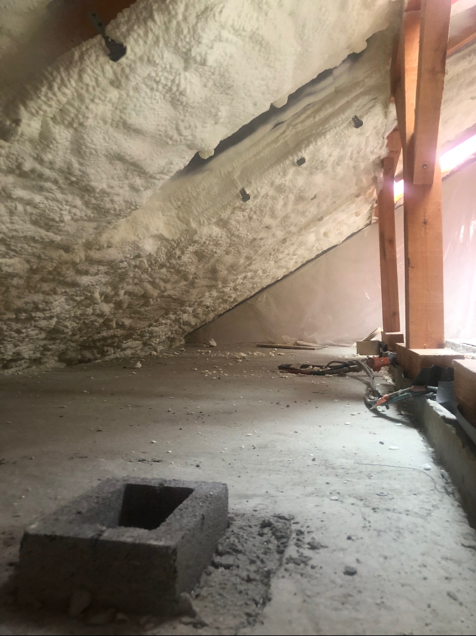 Poddasze w trakcie prac izolacyjnych, pokryte grubą warstwą białej pianki izolacyjnej, z widocznymi elementami konstrukcji drewnianej i narzędziami na betonowej podłodze.