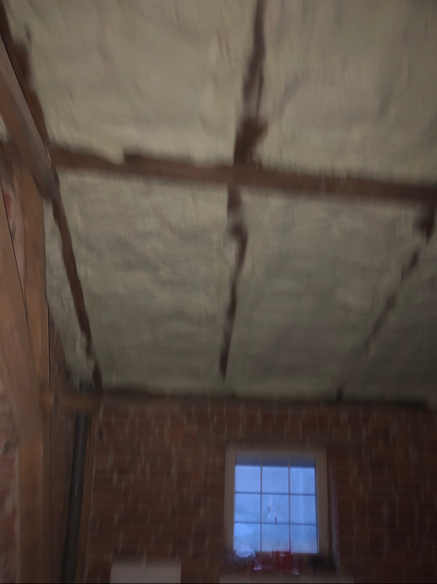 Poddasze z widoczną izolacją pianką PUR, drewniane belki konstrukcyjne i fragment ściany z cegły z oknem.