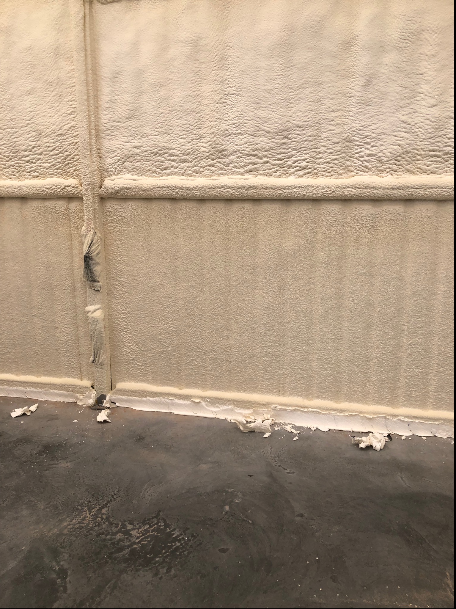 Ściana po ociepleniu pianką PUR, widoczne nierówności struktury pianki i zabezpieczenia na łączeniach. Na podłodze resztki piany po aplikacji.