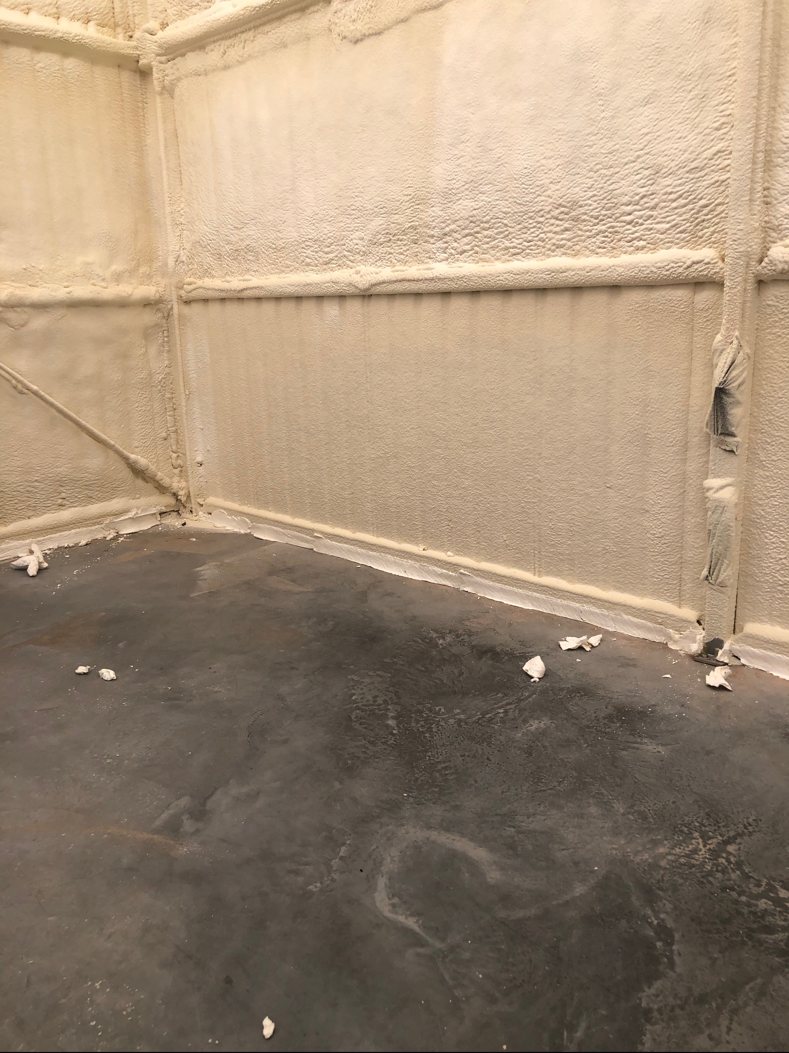 Poddasze po ociepleniu pianką PUR. Widoczne ściany i sufit pokryte warstwą pianki, szczelnie wypełniającą przestrzeń. Szara betonowa podłoga z resztkami pianki.