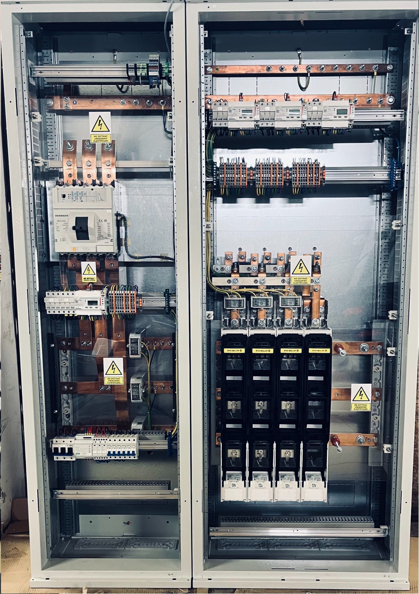 Rozdzielnica elektryczna w szarej obudowie, widoczne bezpieczniki, kable, szyny miedziane i oznaczenia ostrzegawcze. Precyzyjny montaż, estetyczne wykonanie.