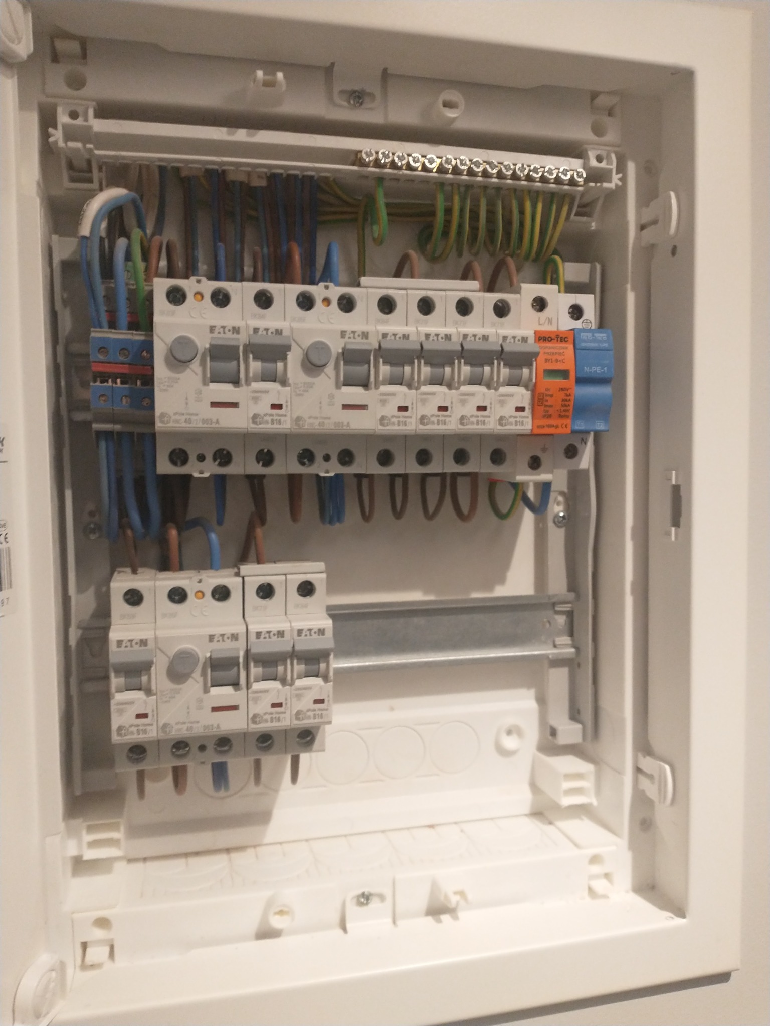 Rozdzielnica elektryczna Eaton z zainstalowanymi bezpiecznikami i przewodami. Widoczne okablowanie w kolorach: niebieskim, brązowym, zielono-żółtym, pomarańczowym.