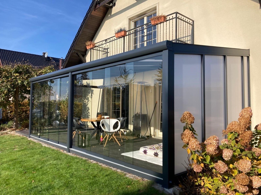 Szklana zabudowa tarasu z metalową ramą w Dobrzeniu Wielkim, widok z zewnątrz na stół i krzesła wewnątrz, obok kwitnące hortensje.