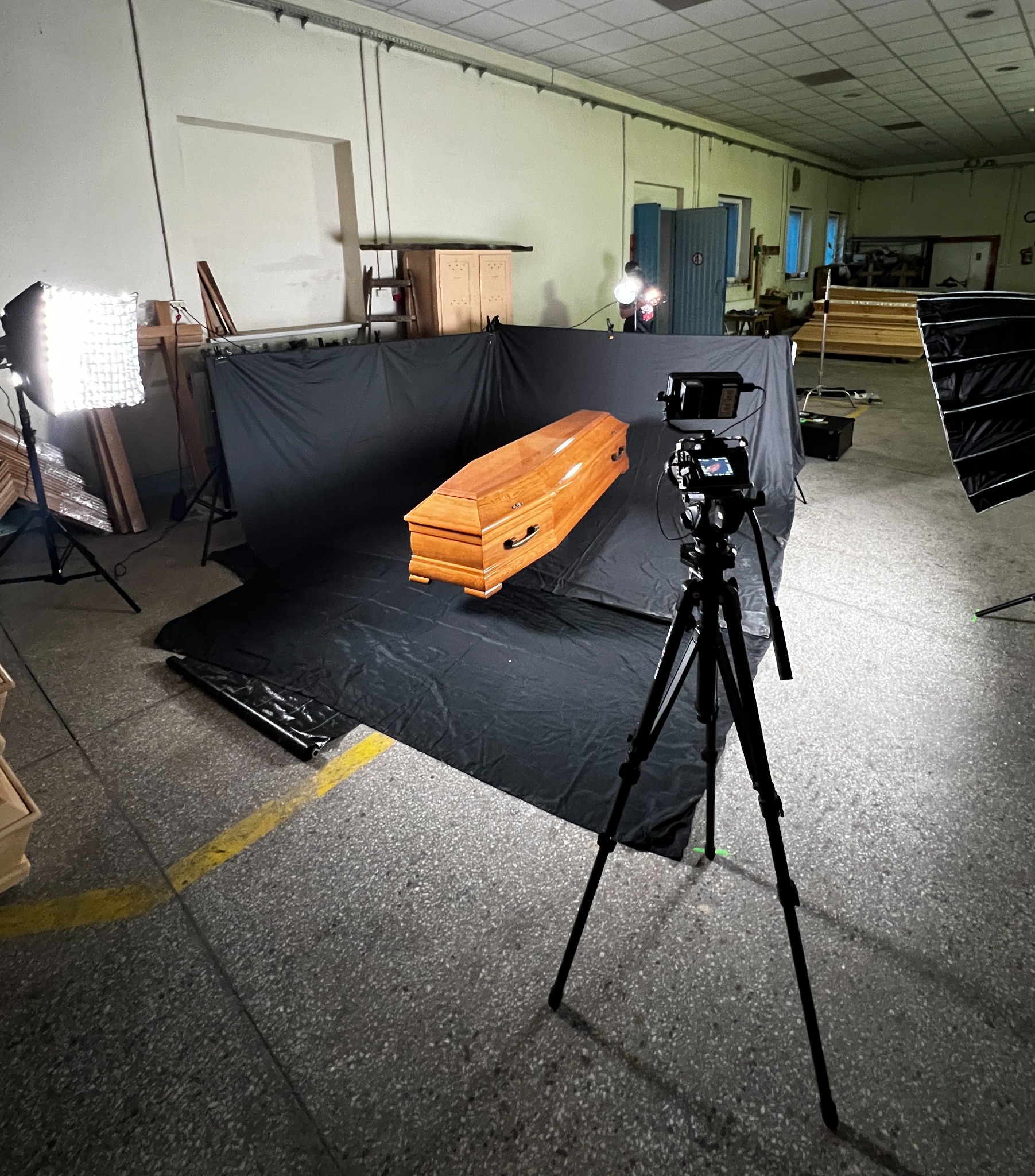 Ujęcie z planu filmowego w Komornikach: lakierowana trumna z metalowymi uchwytami na czarnym tle, oświetlona lampami studyjnymi, nagrywana kamerą na statywie.