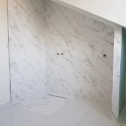 Płytki imitujące marmur na ścianach i podłodze w nowoczesnej łazience z odpływem liniowym, widoczne przygotowane otwory na armaturę.