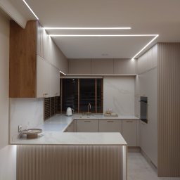 HRS interno sp.zoo - Nowoczesna kuchnia w beżach z marmurowym blatem i oświetleniem LED. Ryflowane fronty szafek i wyspa kuchenna. Minimalistyczny design z elementami drewna.