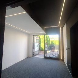 HRS interno sp.zoo - Nowoczesne wnętrze biurowe z oświetleniem LED na suficie, świeżo po malowaniu. Widoczna drabina i osoba w tle, sugerująca prace wykończeniowe.