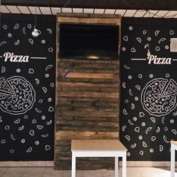HRS interno sp.zoo - Ściana w pizzerii z rysunkami pizzy kredą na czarnej farbie tablicowej, drewniane panele i stoliki. Dekoracja wnętrza lokalu gastronomicznego.