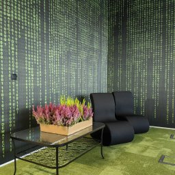 HRS interno sp.zoo - Nowoczesne biuro z tapetą w stylu kodu binarnego, czarne fotele i stolik z kwiatami, tworzące unikalną przestrzeń relaksu.