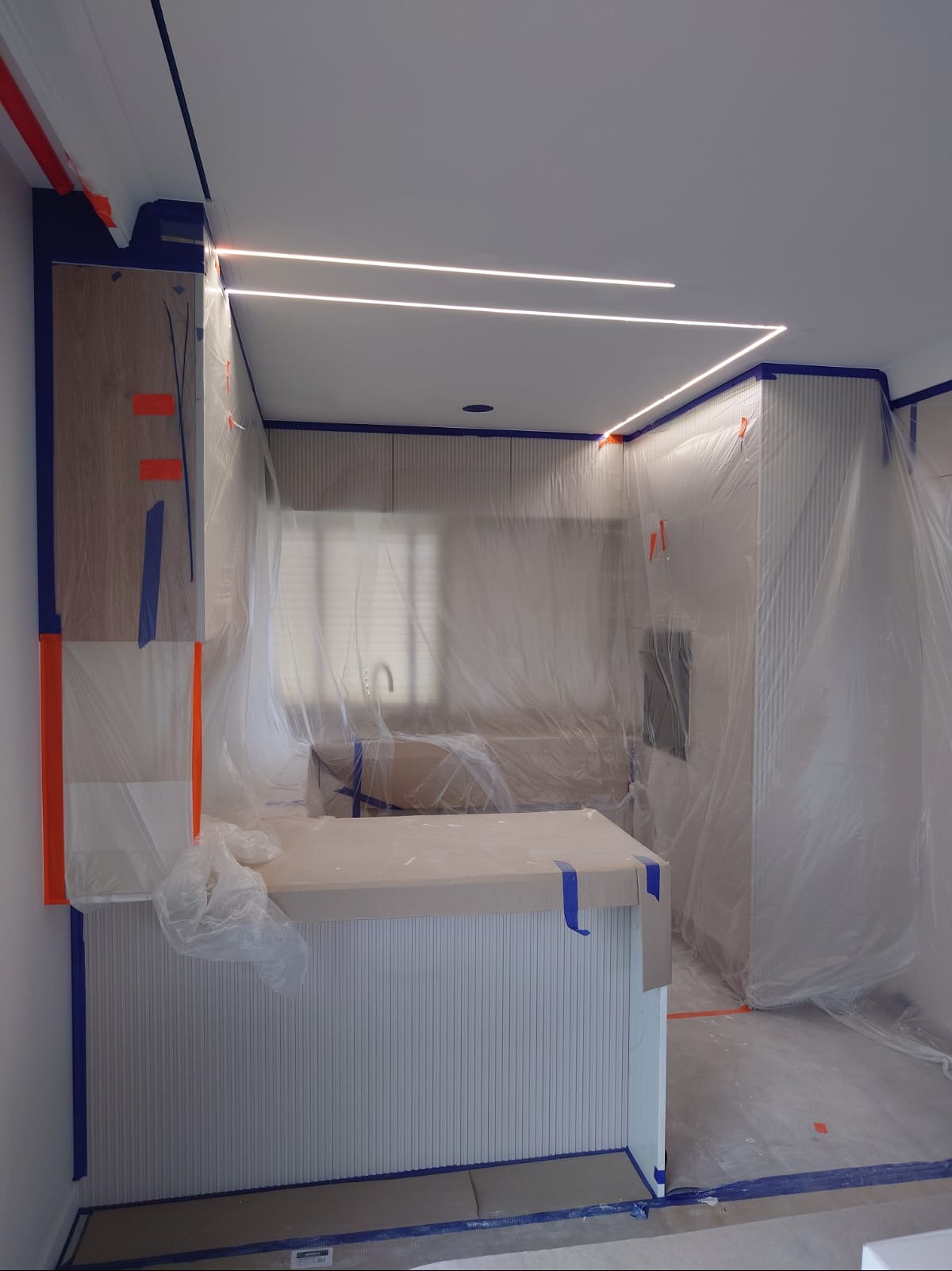 Kuchnia w trakcie zabezpieczania folią i taśmą malarską przed malowaniem. Widoczne oświetlenie LED podszafkowe i listwy dekoracyjne na ścianach.