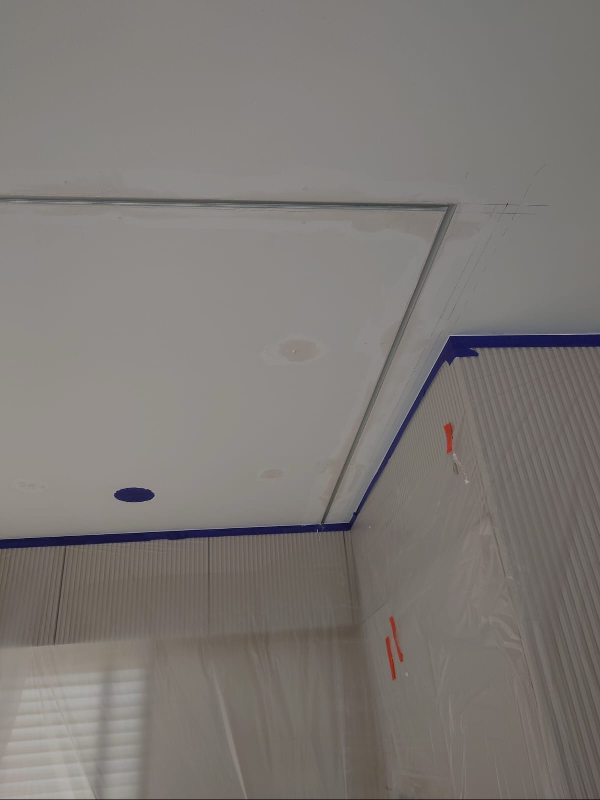 Przygotowanie do malowania sufitu: zabezpieczone ściany folią i taśmą malarską, widoczne ślady po szpachlowaniu i otwór na oświetlenie.