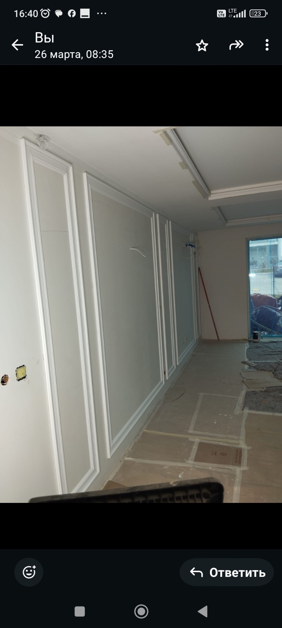 Białe ściany z dekoracyjnymi panelami w trakcie wykańczania wnętrza. Podłoga zabezpieczona kartonem. Widoczne elementy instalacji elektrycznej.