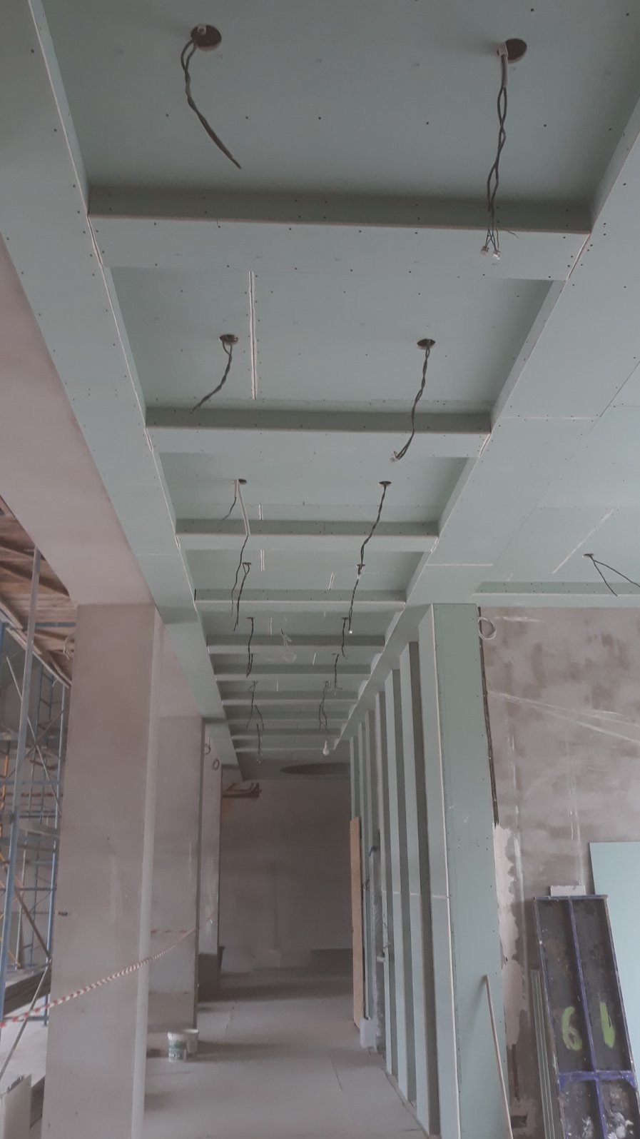 Sufit podwieszany z płyt karton-gips z widocznymi przewodami elektrycznymi, w trakcie montażu. Widok z dołu, surowy stan wykończenia wnętrza.
