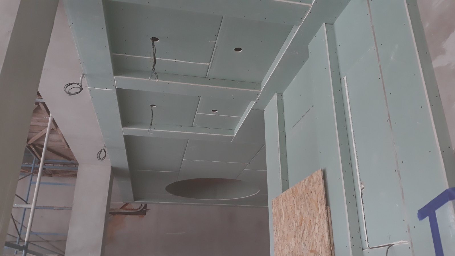 Sufit podwieszany z płyt kartonowo-gipsowych w trakcie montażu, widoczne otwory na oświetlenie i kable, ściany również pokryte płytami, surowe wykończenie.