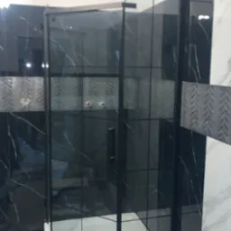 Nowoczesna kabina prysznicowa z czarnymi profilami i marmurowymi płytkami na ścianach, widoczne białe fugi i odpływ liniowy w brodziku.