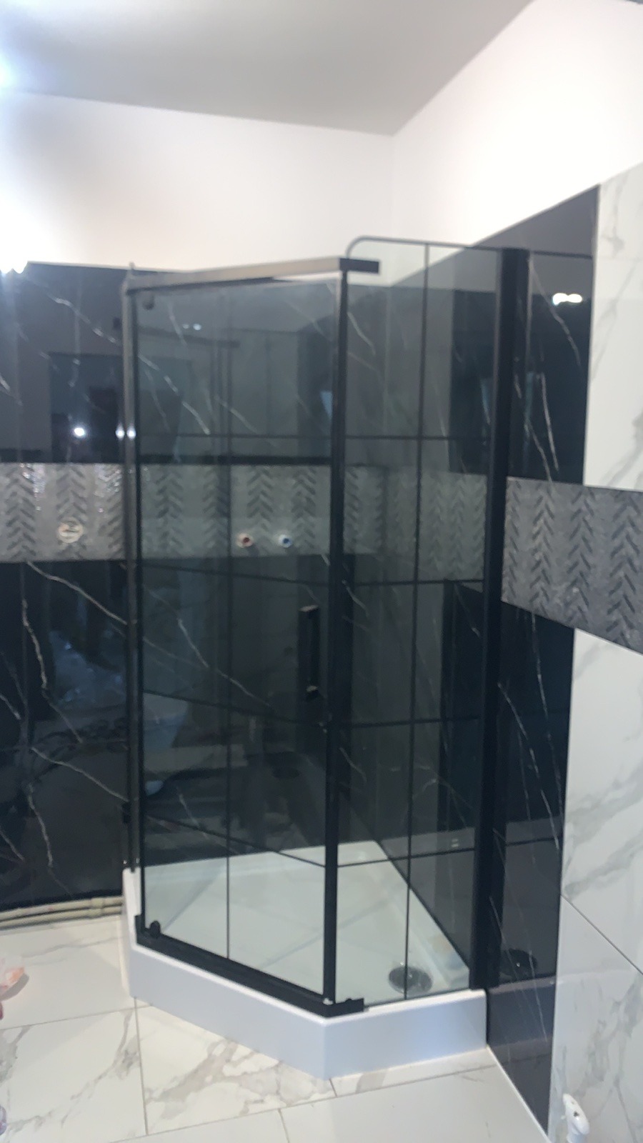 Nowoczesna kabina prysznicowa z czarnymi profilami i marmurowymi płytkami na ścianach, widoczne białe fugi i odpływ liniowy w brodziku.