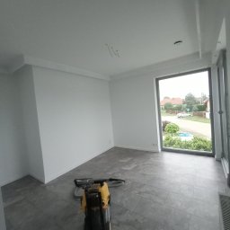 Bigbud - Wnętrze pomieszczenia po malowaniu ścian na biało, widoczna maszyna do czyszczenia posadzek na szarych płytkach, duże okno z widokiem na ulicę.