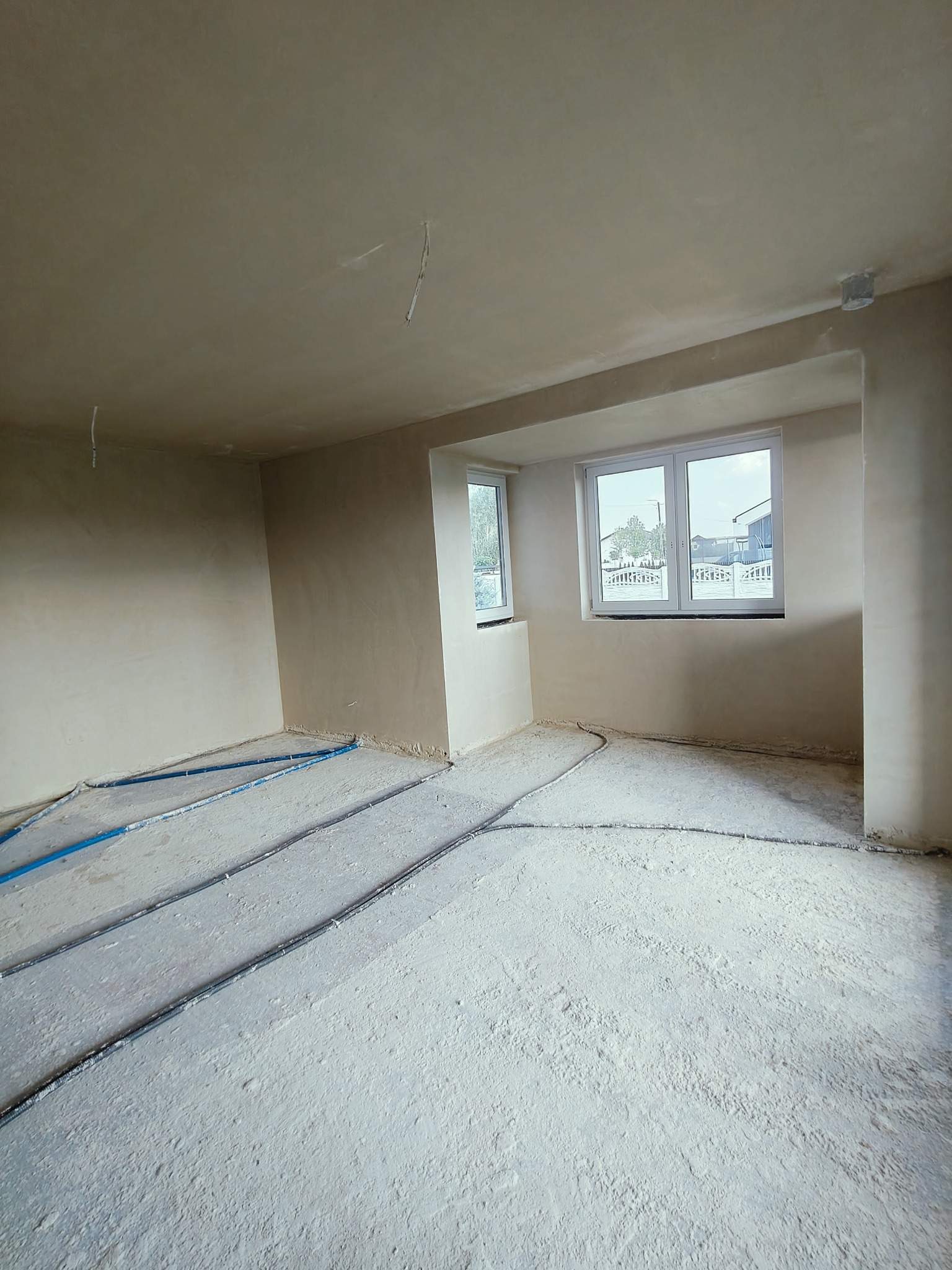 Pokój w trakcie prac wykończeniowych, ściany pokryte świeżym tynkiem, na podłodze rozprowadzone rury ogrzewania podłogowego.