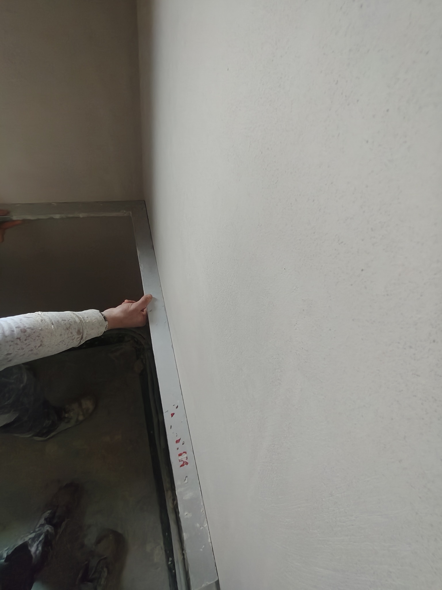 Ściana po nałożeniu gładzi, widoczna ręka przy futrynie. Delikatna faktura, jasny odcień szarości. Praca w trakcie wykończenia.