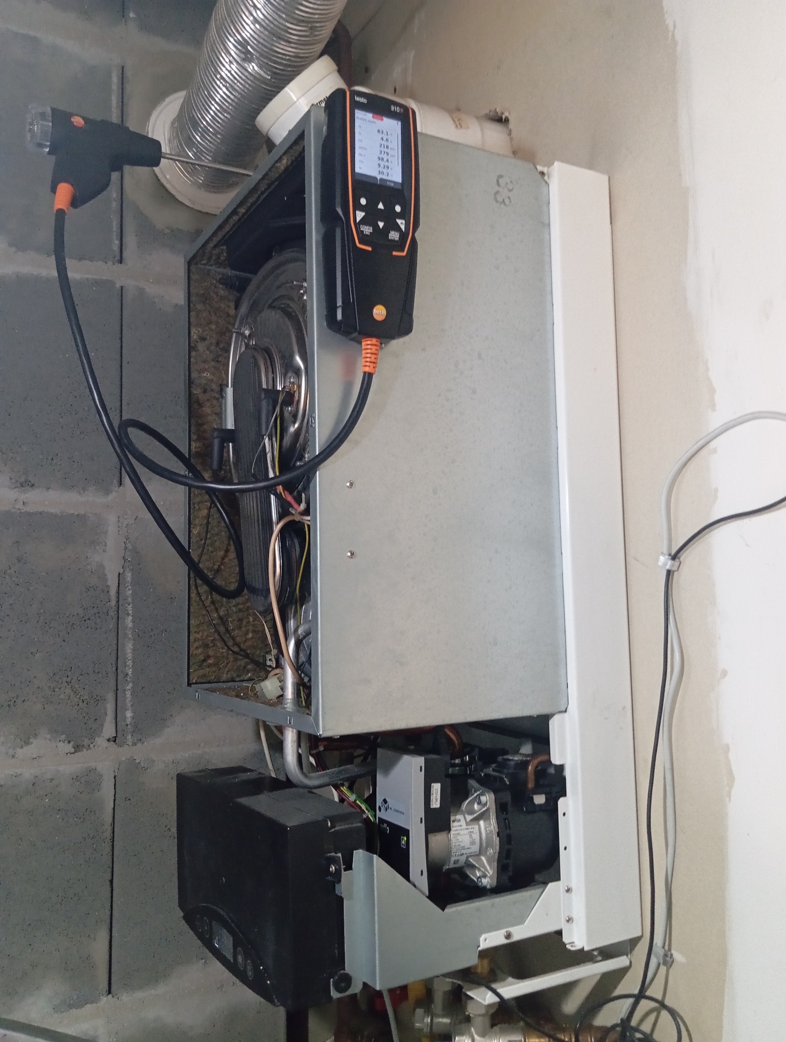 Analizator spalin Testo 310 mierzy parametry pieca gazowego, rura spalinowa z aluminium karbowana widoczna w tle.