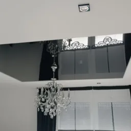 Nowoczesny salon z czarnym, lustrzanym sufitem podwieszanym i kryształowym żyrandolem. Widoczne punktowe oświetlenie i okna z czarnymi zasłonami.