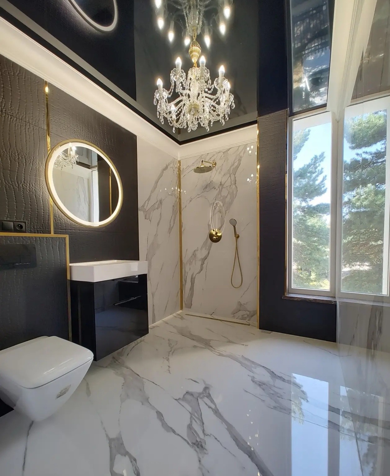 Luksusowa łazienka z marmurową podłogą i ścianami, okrągłym lustrem z podświetleniem LED, kryształowym żyrandolem i kabiną prysznicową typu walk-in.