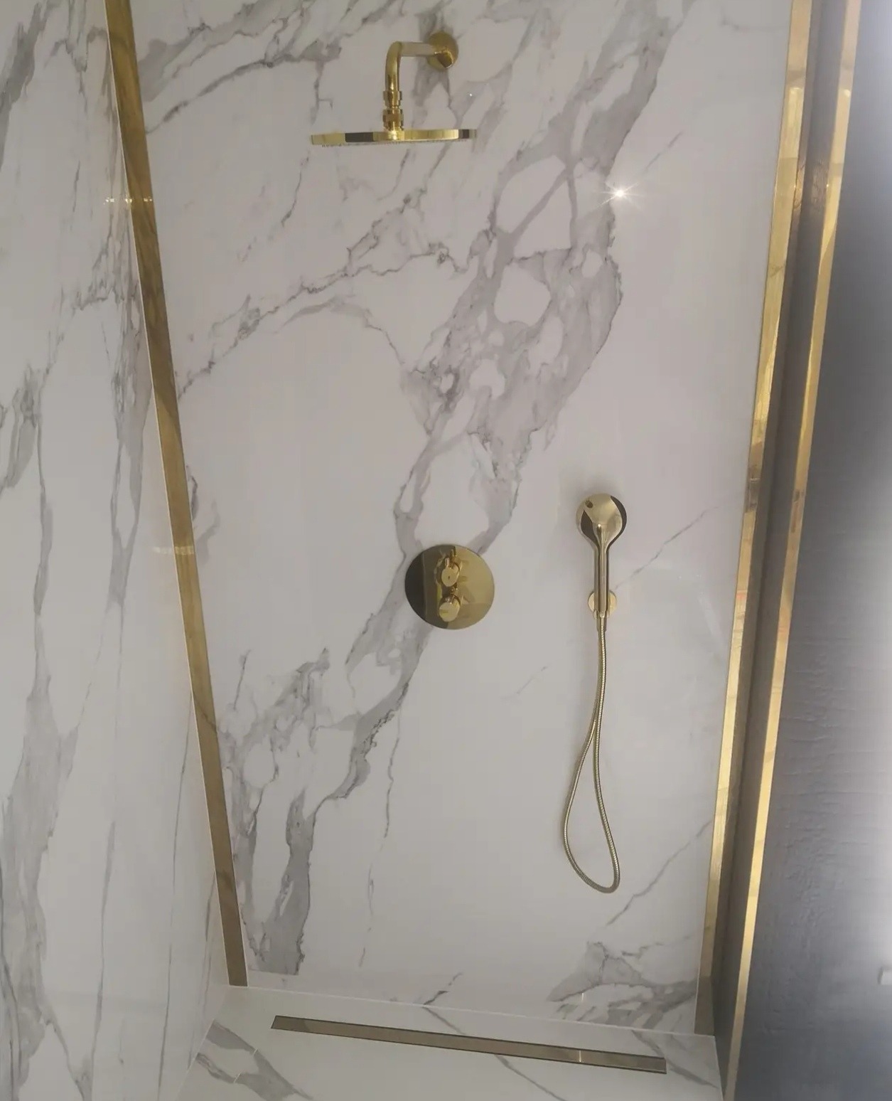 Wykończona kabina prysznicowa z marmurowymi płytkami i złotą armaturą, widok z dołu, podkreślający luksusowy charakter. Minimalistyczny design z dbałością o detale.